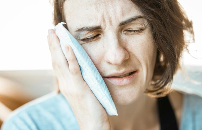 Acil diş ağrısı yaşayan bir bireyin yüz ve çene bölgesini tutarken gösteren bilgilendirici görsel.